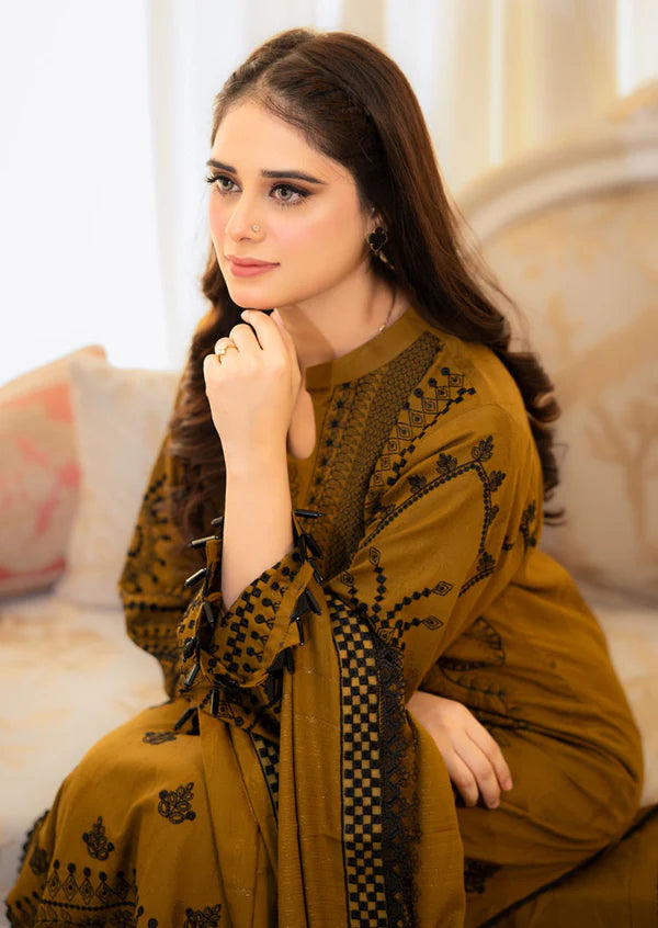 Woman wearing a mustard yellow traditional outfit with black patterns, sitting on a couch.